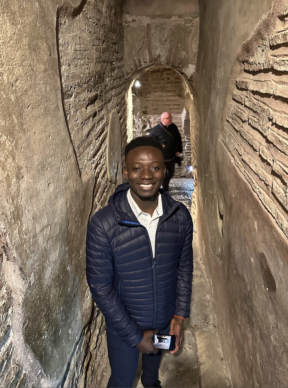 Standing in a narrow vaulted stone passage, another visitor on the steps behind.