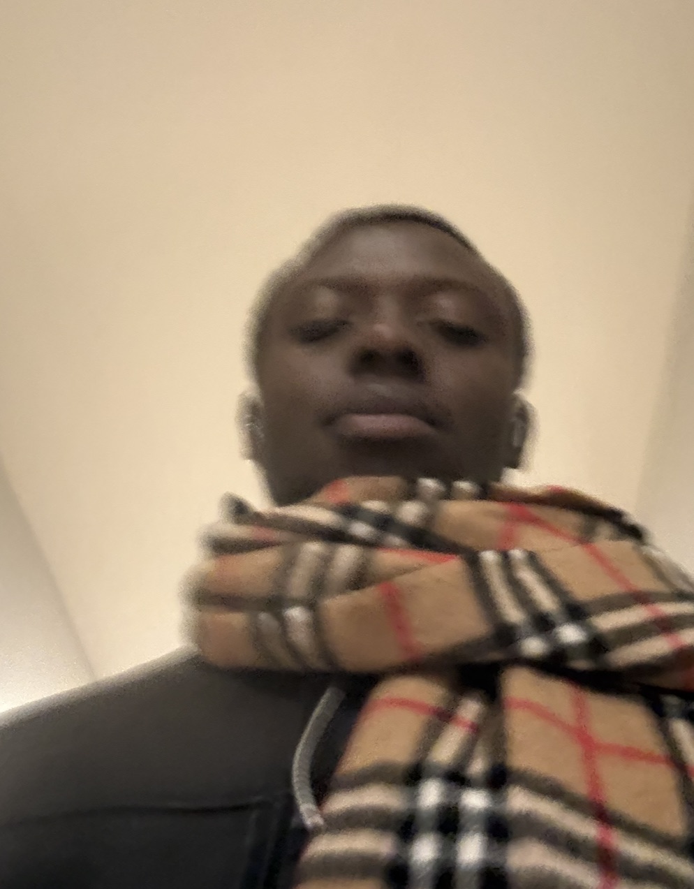 Motion-blurred selfie in a dark coat and a beige check scarf.