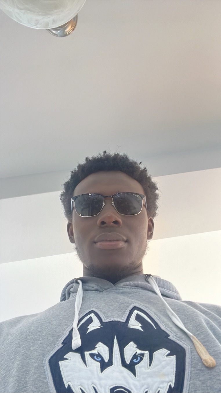 Selfie indoors in sunglasses and a grey UConn husky hoodie.